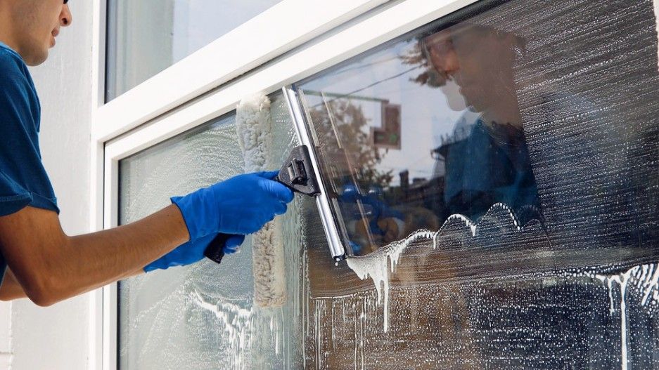A Man is Cleaning a Window With a Squeegee — Verdi Cleaning Services in Belconnen, ACT