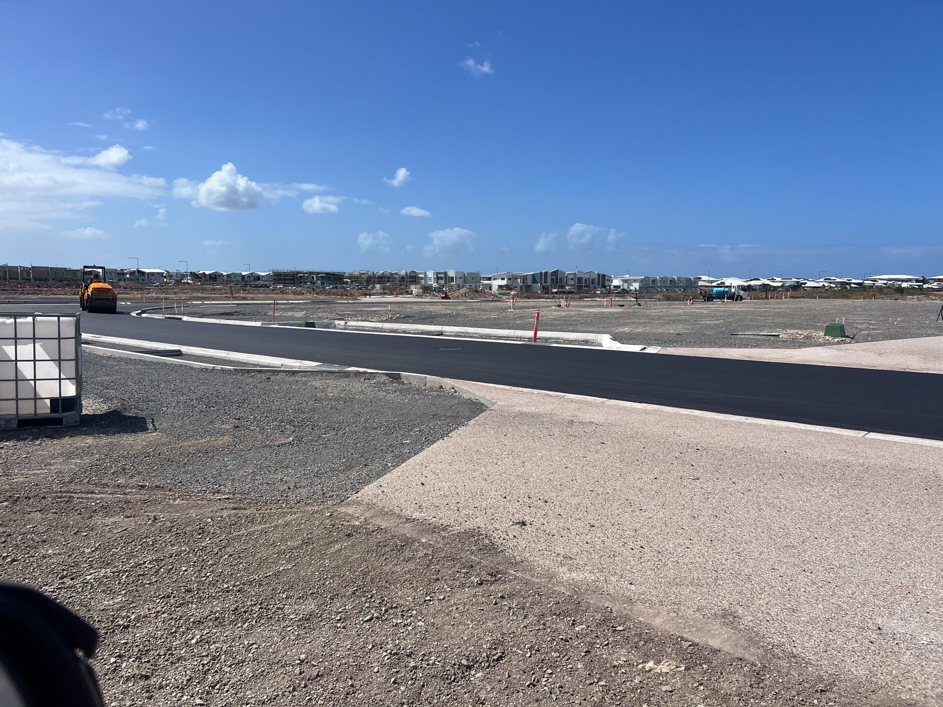 Construction site with paved road and heavy machinery under a bright blue sky.