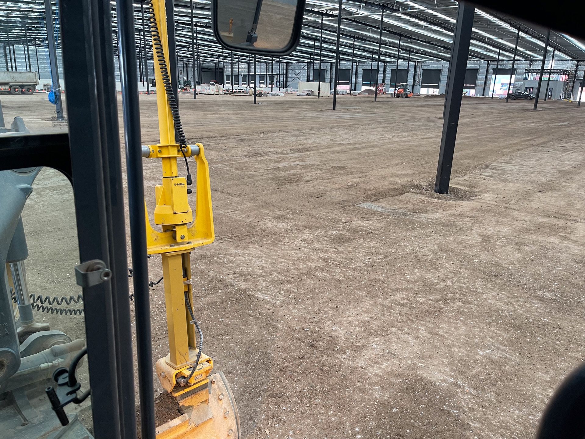 Interior view of a construction site. A yellow backhoe arm and exposed steel beams inside a large building.
