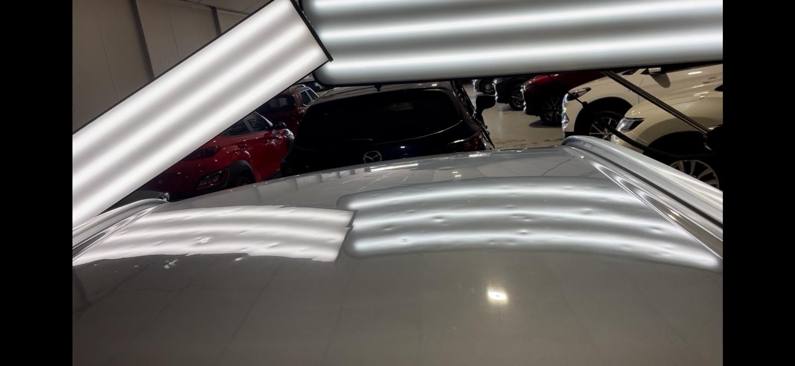 Person using a tool to repair a dent on a black car roof in a well-lit shop.