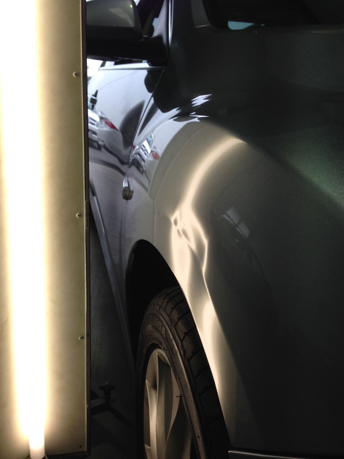 Silver car with a large dent in the passenger side door, parked on asphalt.