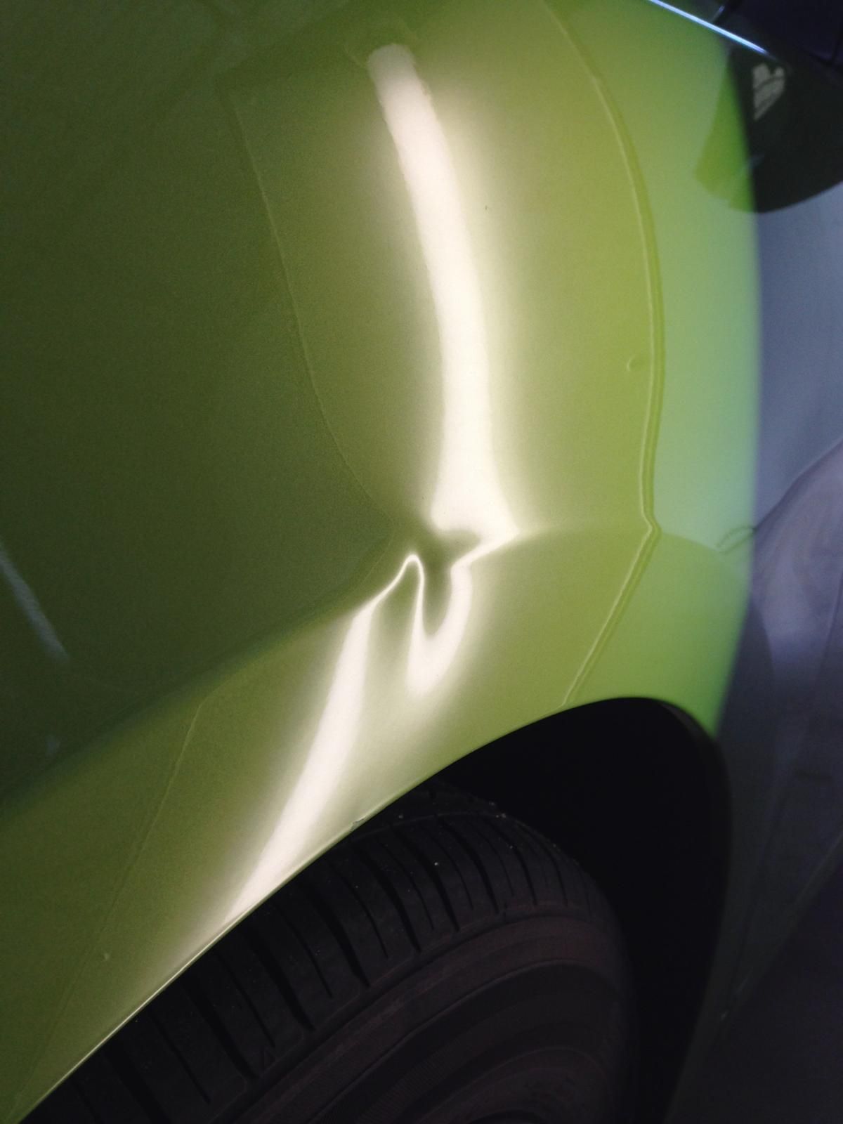 Damaged white car panel with a dent near the tire, labeled 