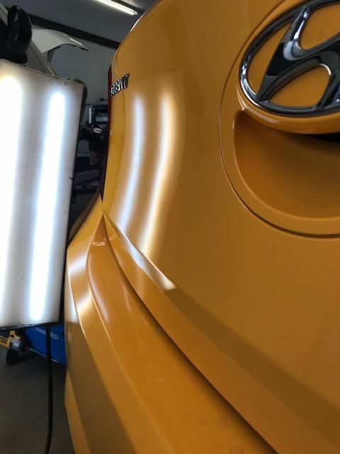 White car fender dented above tire, with reflective light lines.