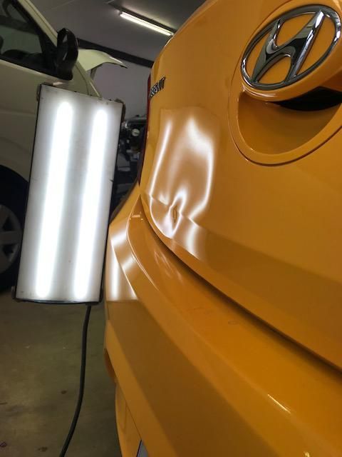 White car fender with a large dent above the tire.