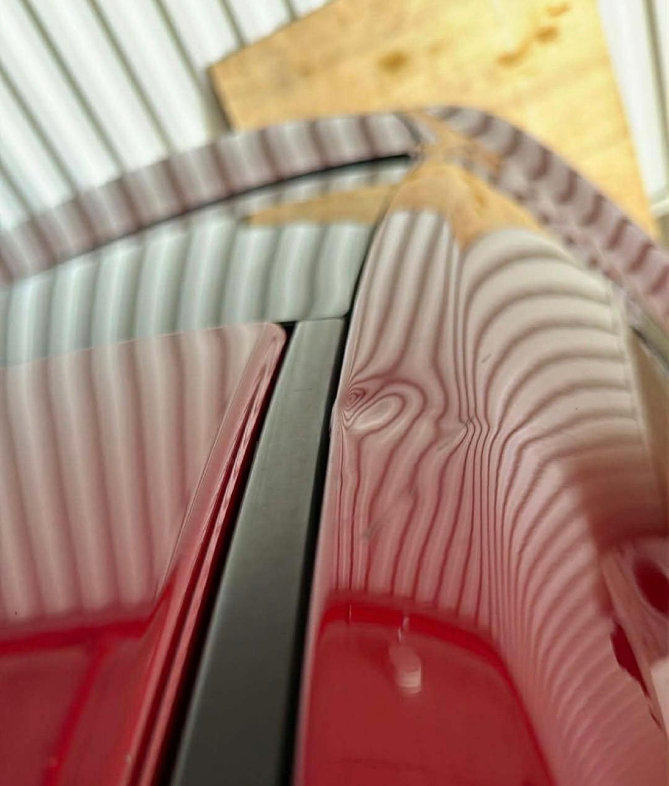 Person using a tool to repair a dent on a black car roof in a well-lit shop.