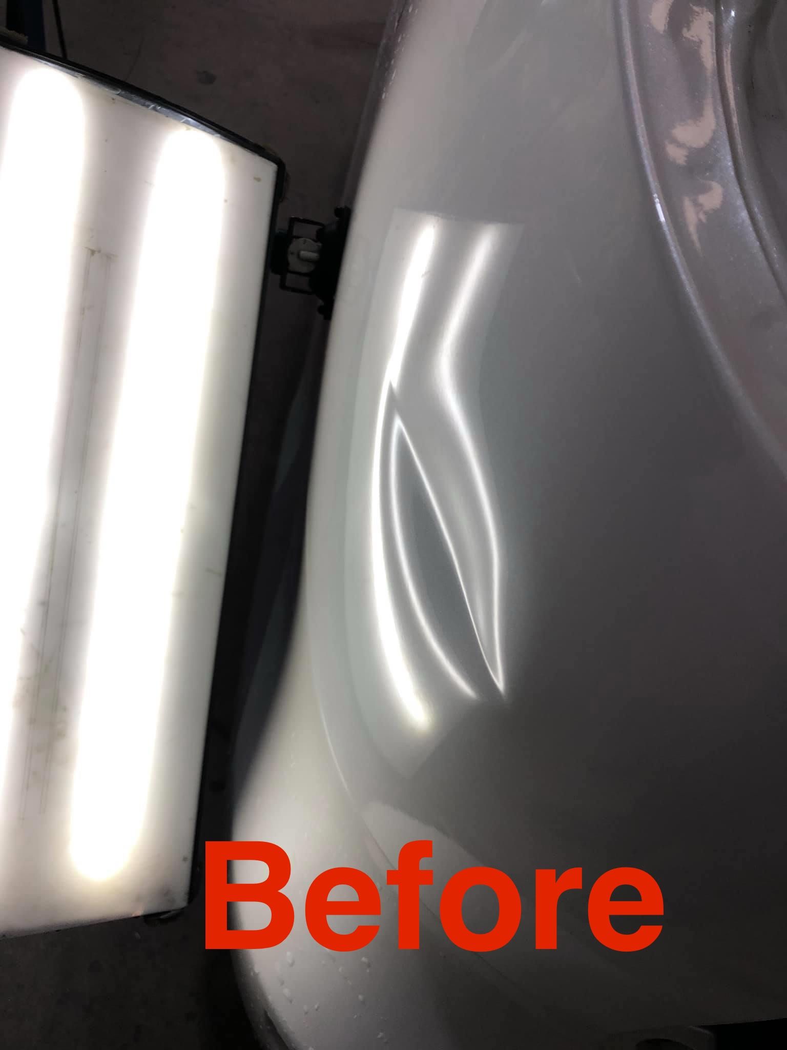 White car fender with a dent, shown before dent repair, reflected in a light panel.