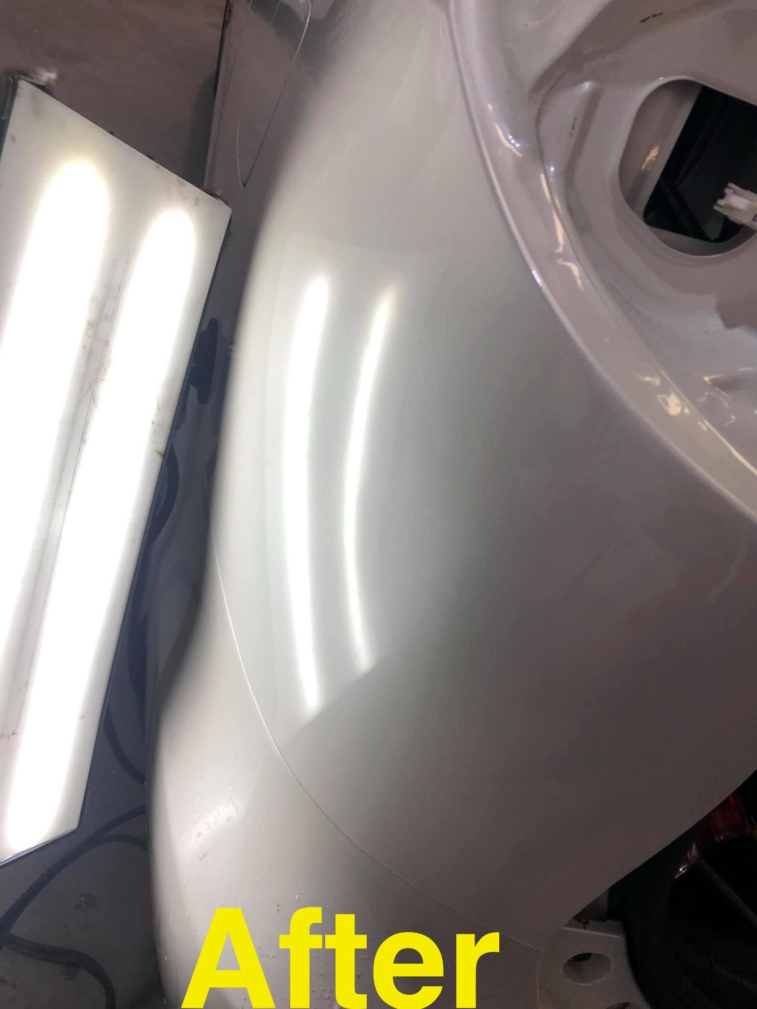 White car fender with a smooth, glossy finish after repair, reflecting bright lights.