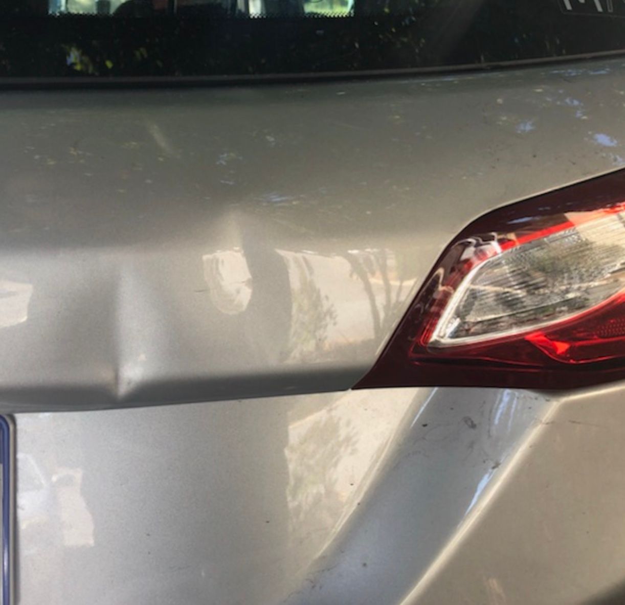 Close-up of a damaged, tan pickup truck bed with rust near the top and a black handle.