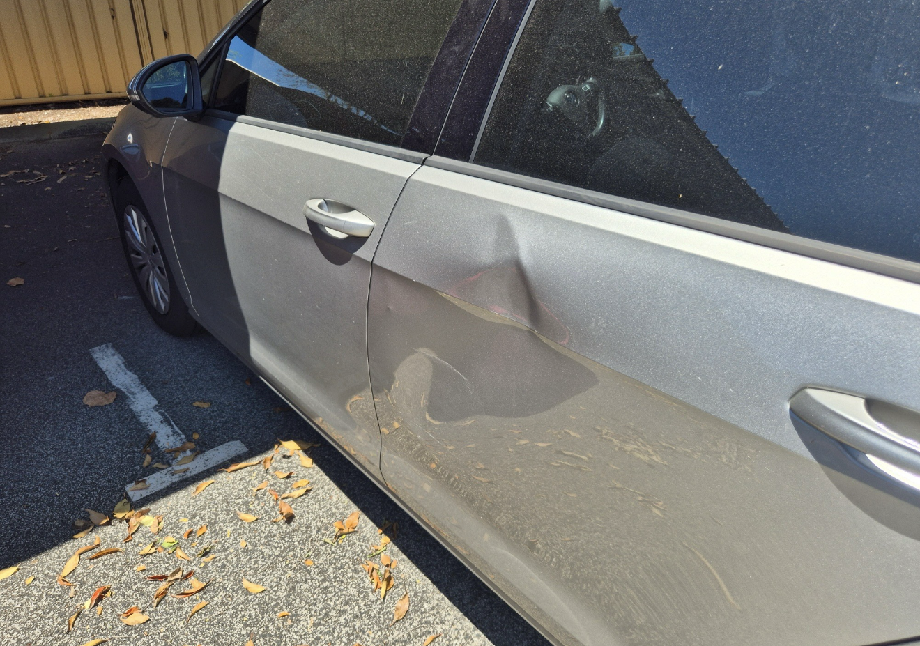 Silver car with a large dent in the passenger side door, parked on asphalt.