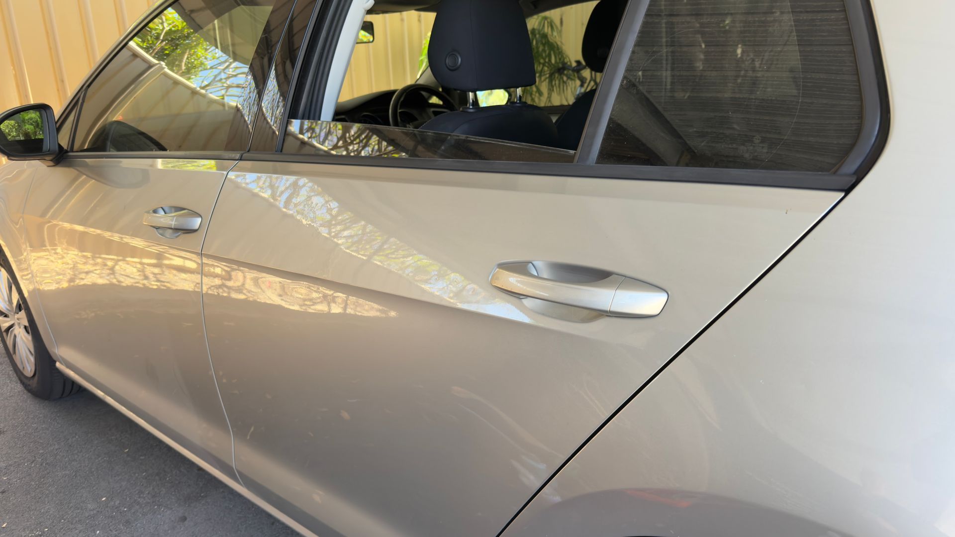 Tan car parked under a shaded structure; rear door and side visible.