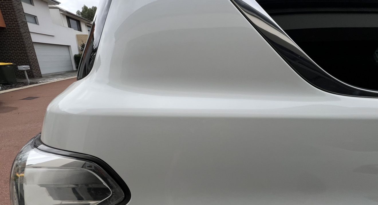 White car rear quarter panel with taillight, parked in driveway.