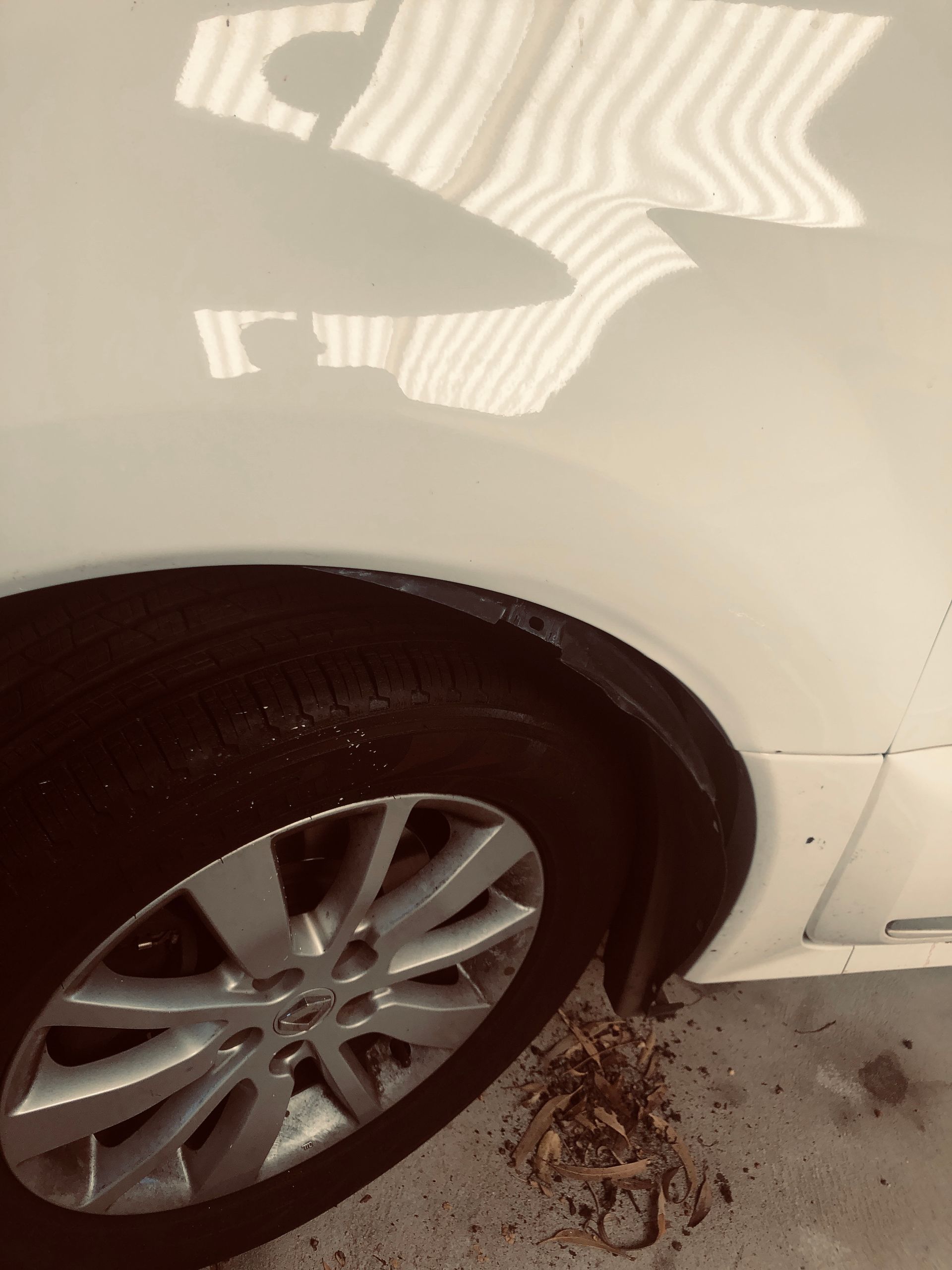 White car fender dented above tire, with reflective light lines.