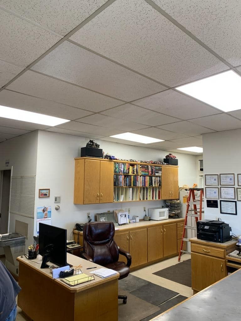 Office interior: desk, cabinets, chair, files, printer, computer, and a suspended ceiling with lighting.