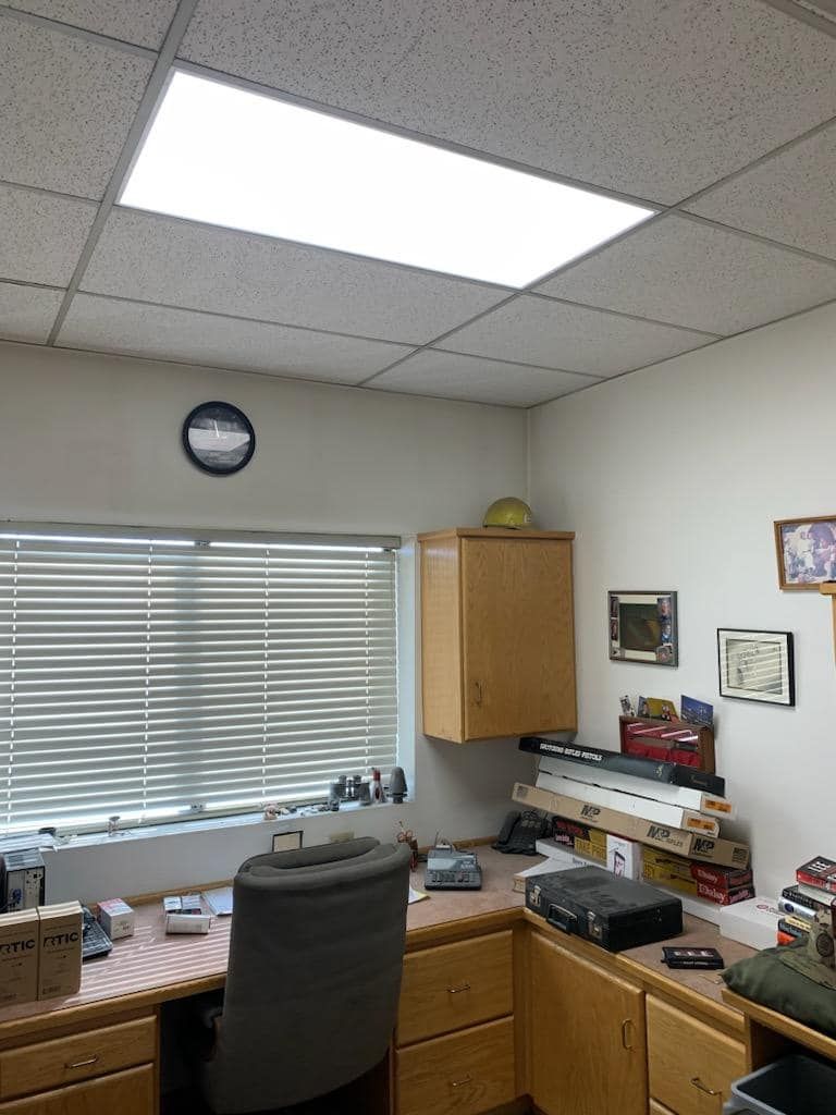 Office interior with desk, window, overhead lighting, cabinets, and various items.