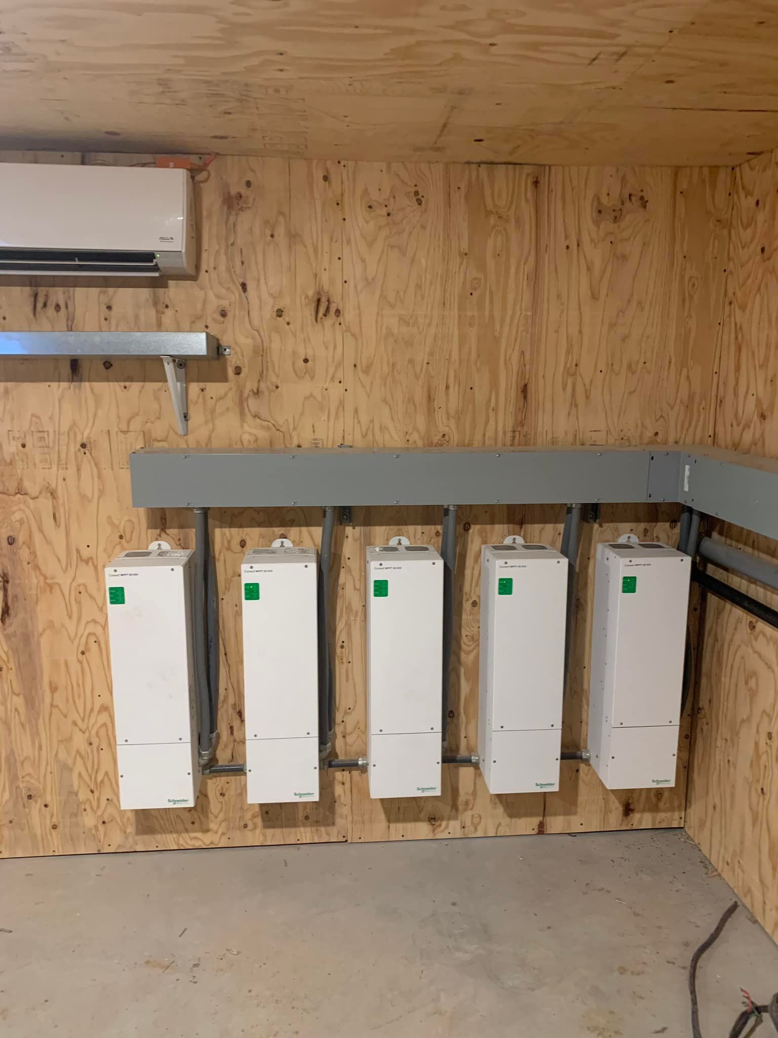 Five white electrical boxes mounted on a wood wall, with a metal bar above them, and an air conditioner.