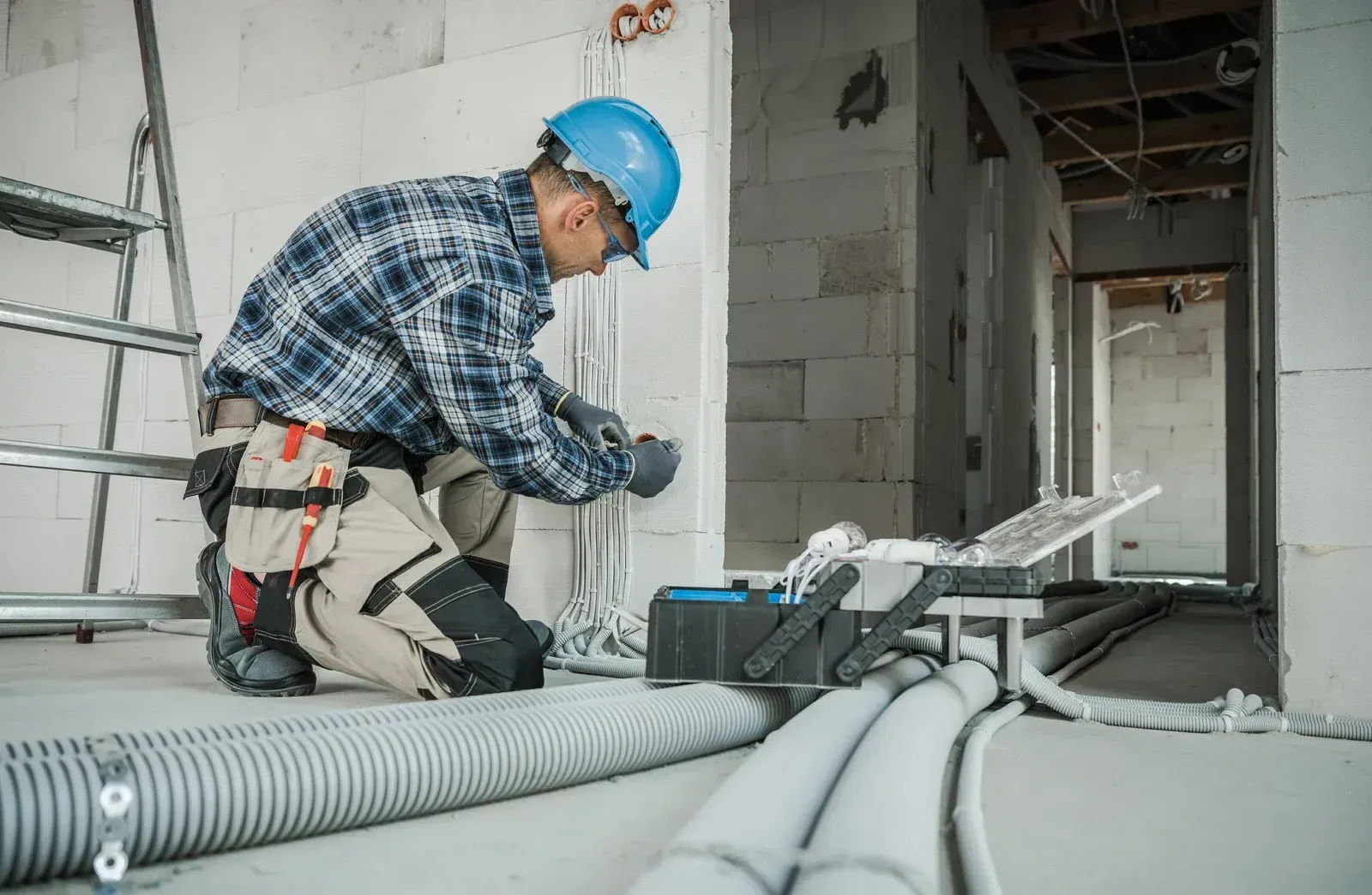 Electrician in blue helmet, installing wires in a new construction.