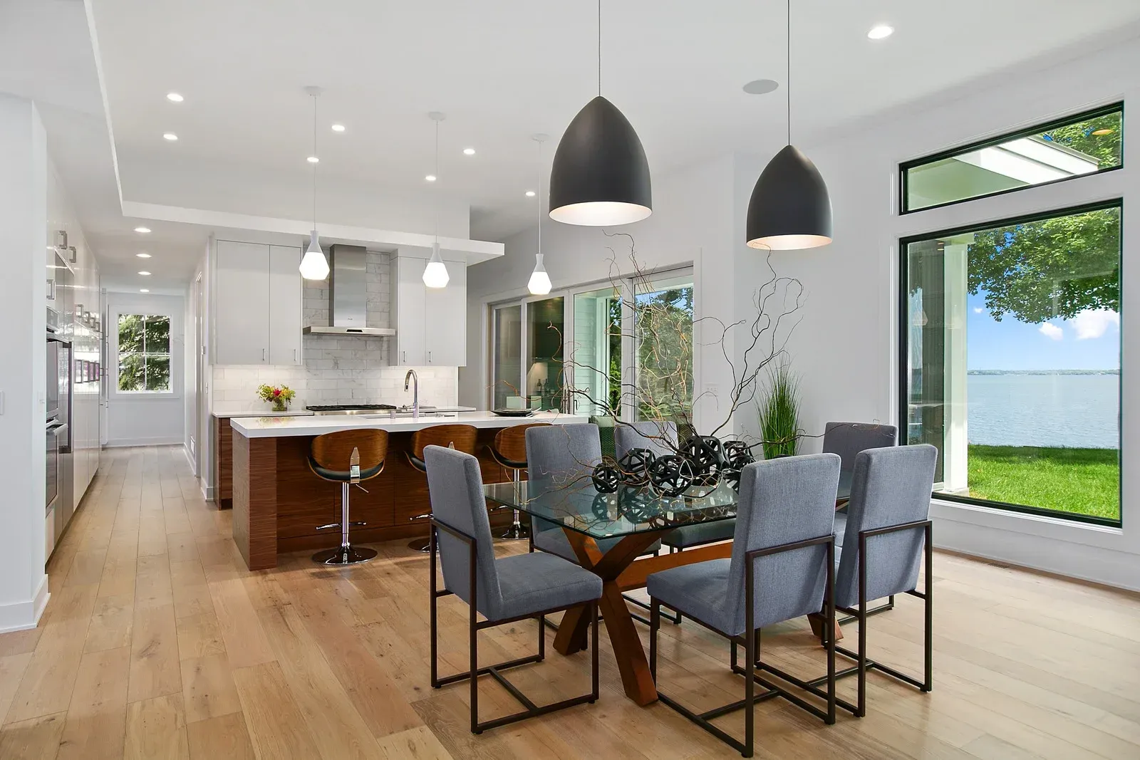 Modern kitchen and dining room with wood floors, island, glass table, and pendant lights.