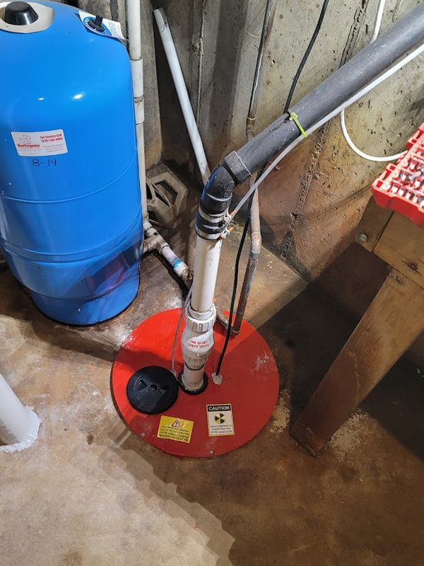 A red sump pump is sitting in a basement next to a blue tank.
