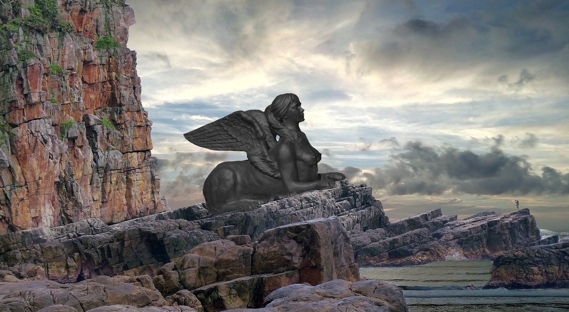 A statue of a sphinx sitting on top of a rocky cliff near the ocean.