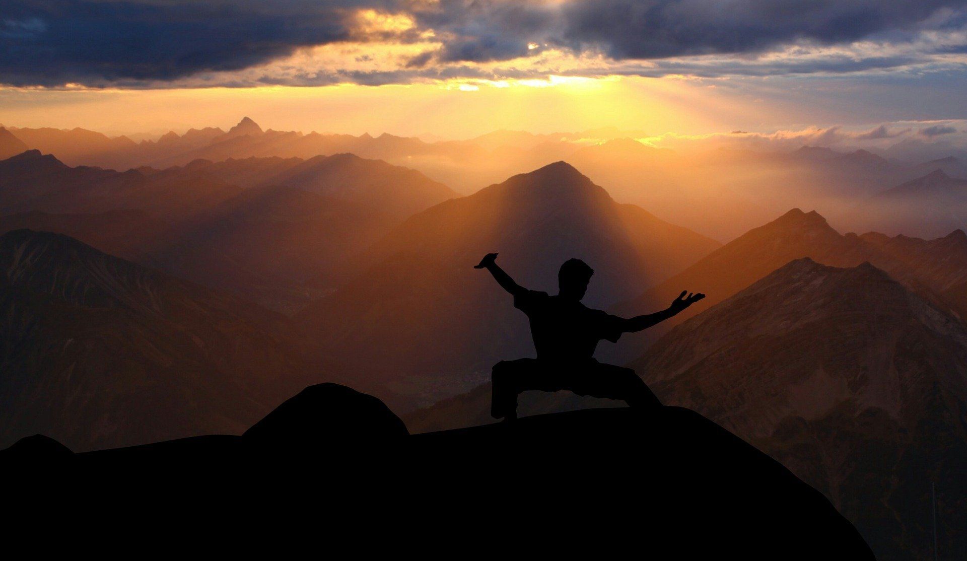 A man is standing on top of a mountain at sunset.