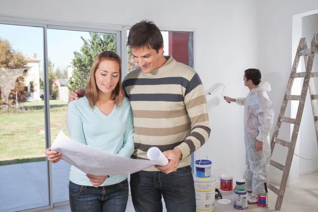 a man and a woman are looking at a blueprint in a room that is being painted