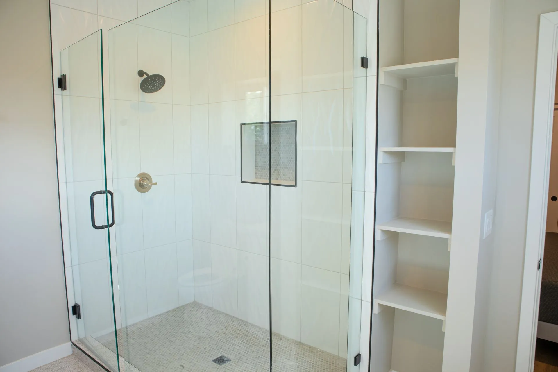 A bathroom with a walk in shower with a glass door and shelves.