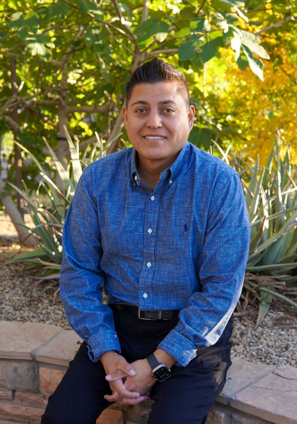 A man in a blue shirt is sitting on a stone wall.