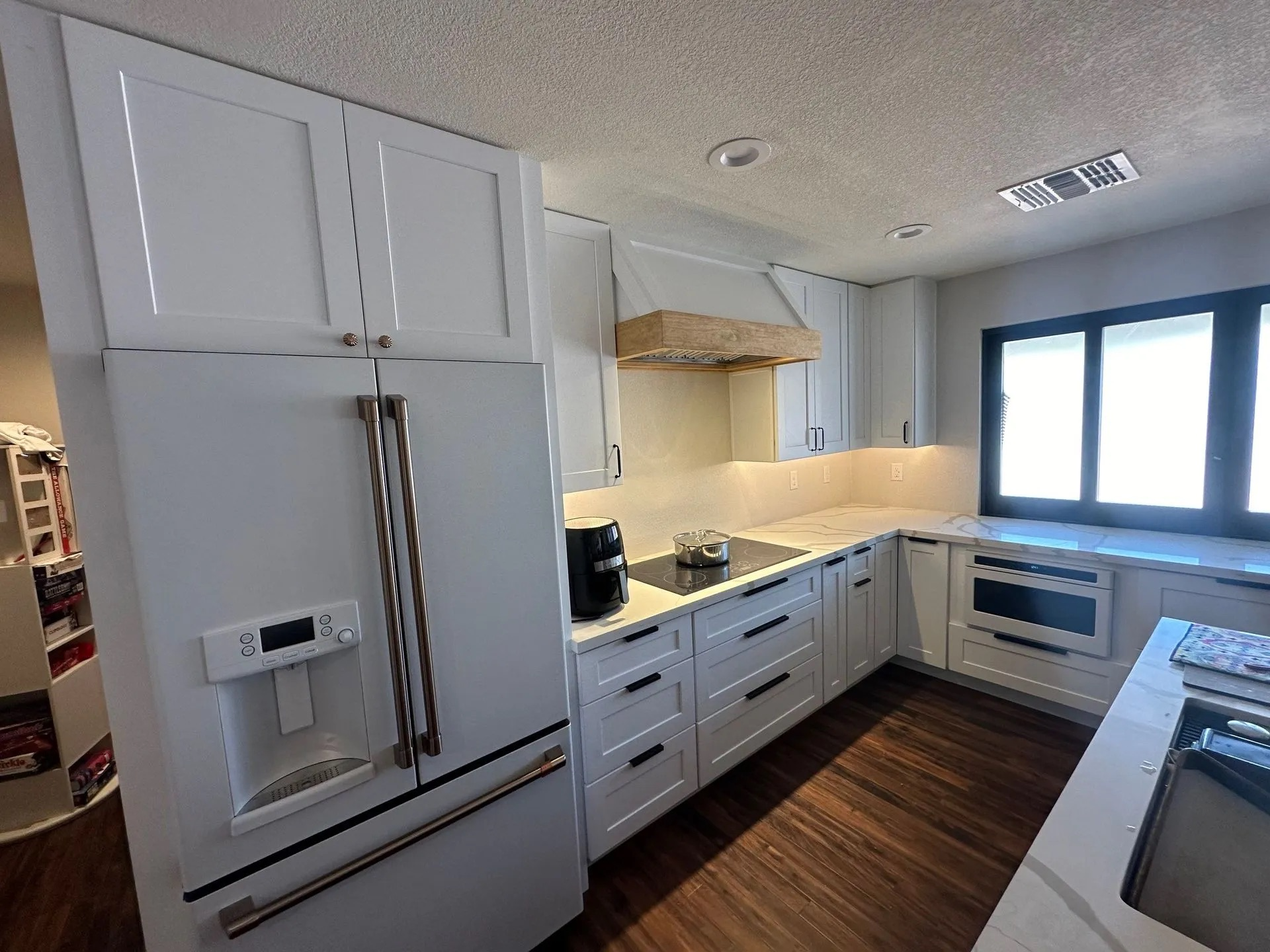 A kitchen with white cabinets , a refrigerator , a stove , and a window.
