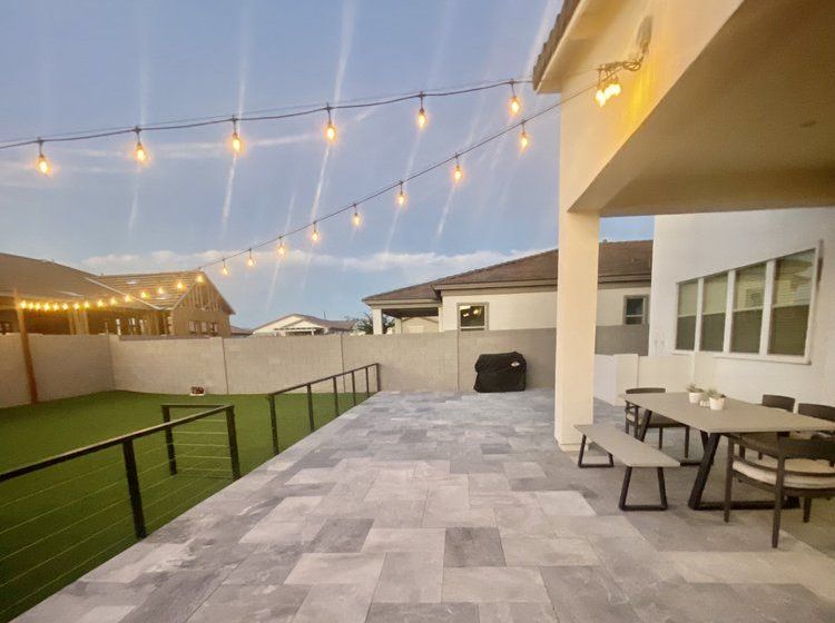 A patio with a table and benches and a string of lights hanging from the ceiling.