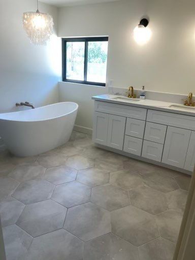A bathroom with a tub , sinks , cabinets and a window.