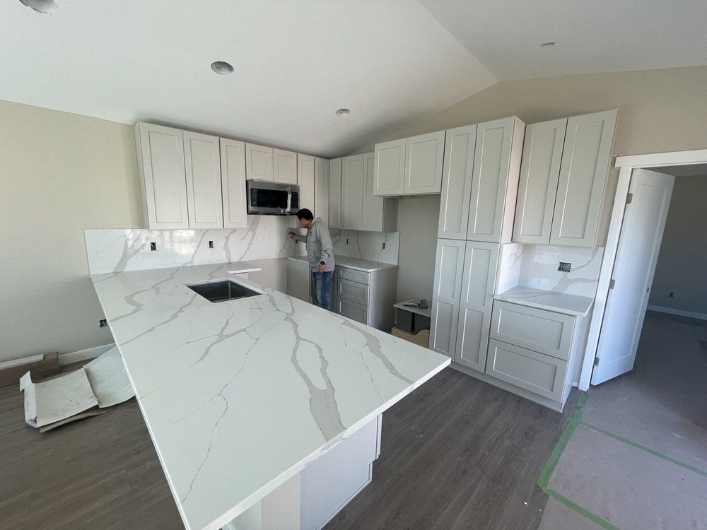 A man is standing in a kitchen with white cabinets and a large island.