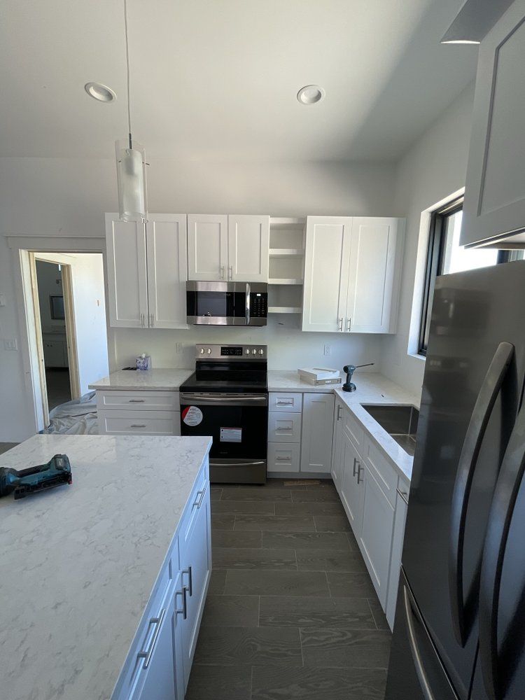 A kitchen with white cabinets , a stove , microwave , refrigerator and sink.