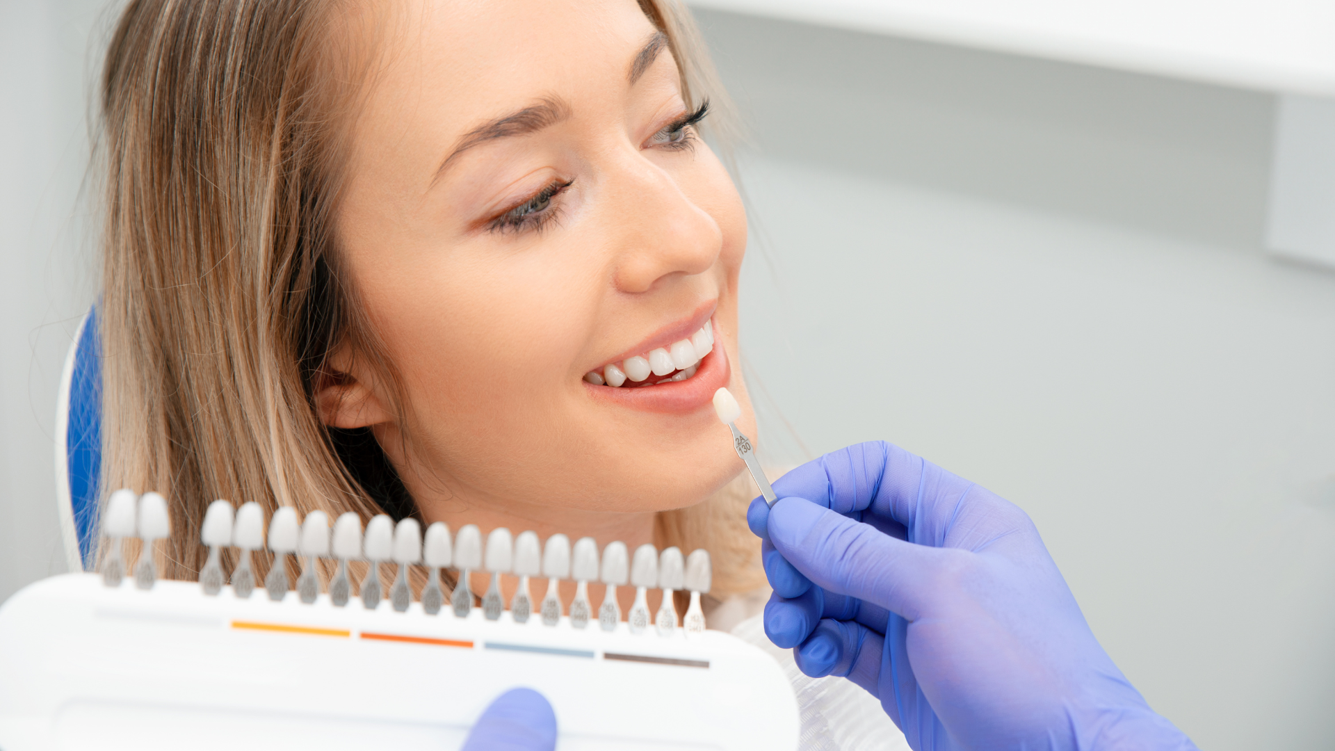 A woman is sitting in a dental chair while a dentist examines her teeth.