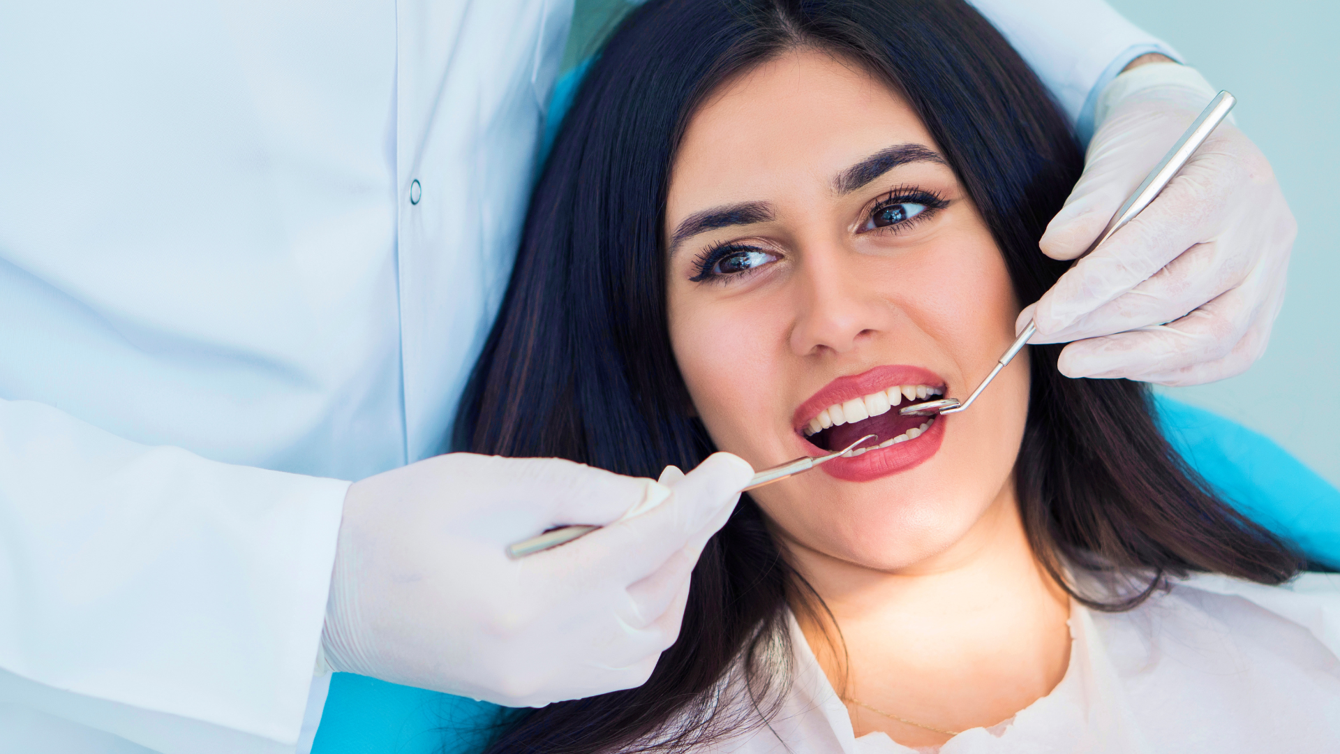 A woman is sitting in a dental chair getting her teeth examined by a dentist.