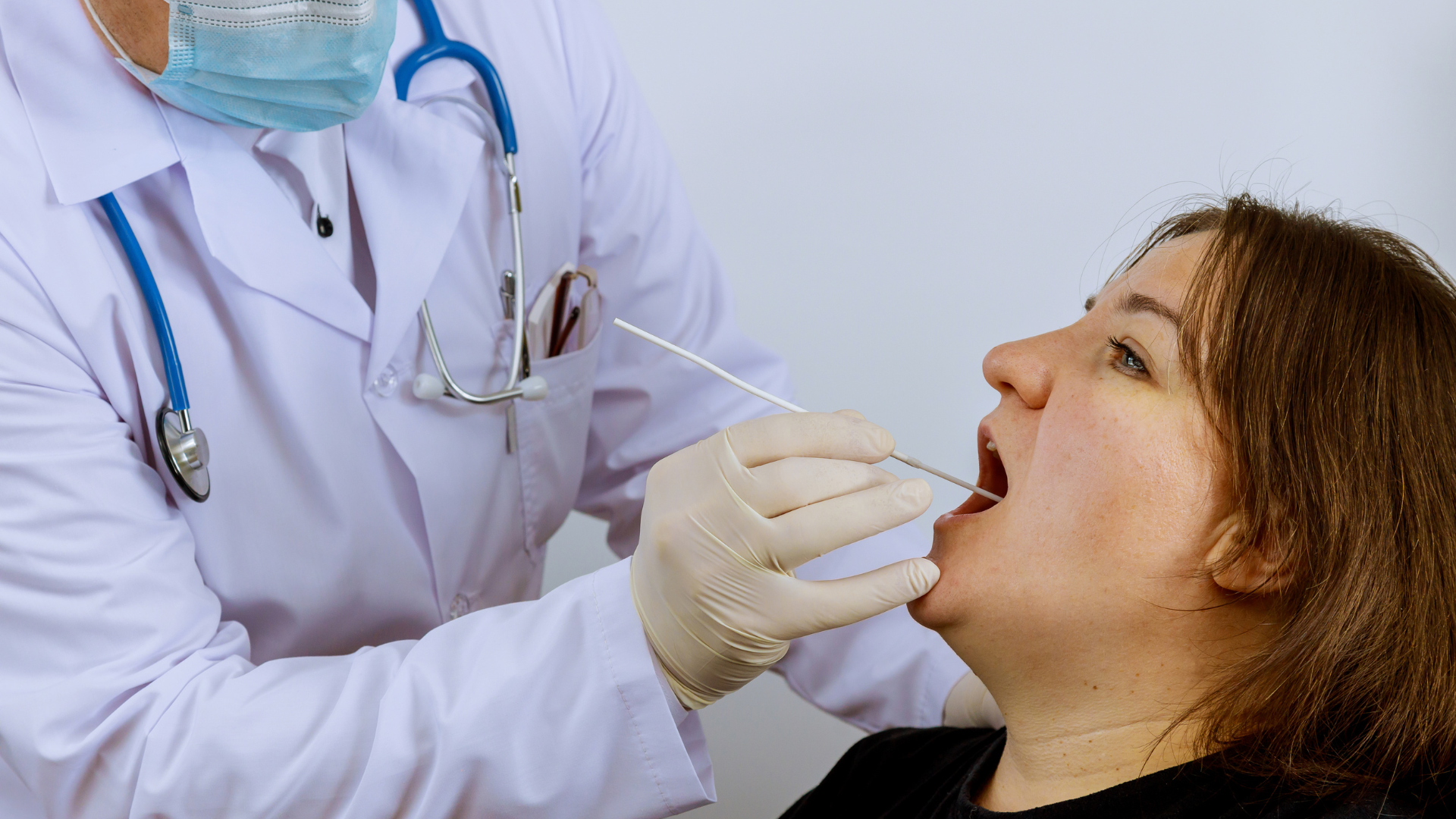 A doctor is taking a sample from a woman 's mouth.