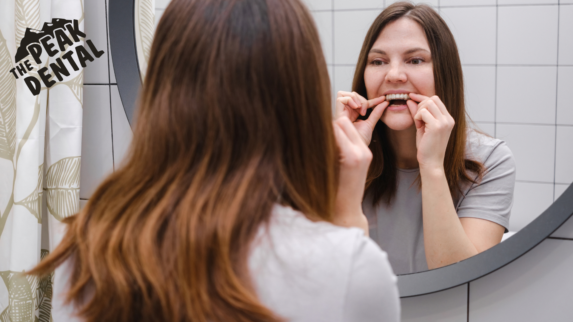 A woman is brushing her teeth in front of a mirror.