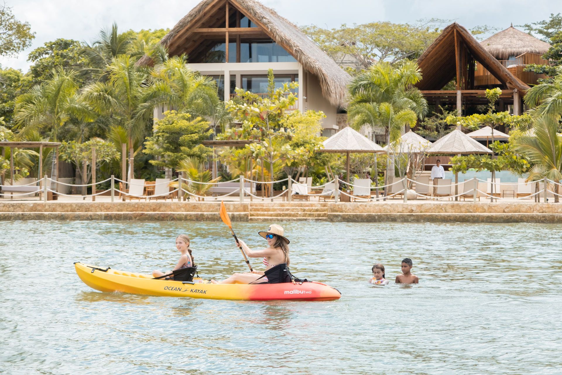 san antero con kayak amarillo sobre el agua, huéspedes nadando y hotel con palmeras frente a la playa
