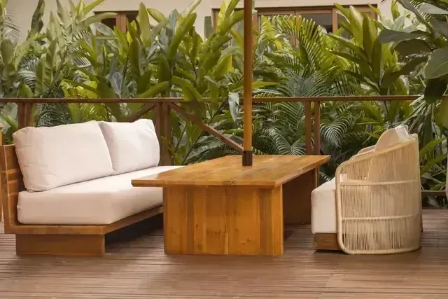Terraza lounge del Hotel Aimarawa con sofás acolchados, mesa de madera y sillas artesanales, rodeada de exuberante vegetación tropical.
