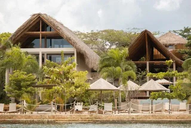 Vista exterior del Hotel Aimarawa frente al mar Caribe con cabañas de lujo en palma y madera, rodeadas de palmeras y zona de playa privada.