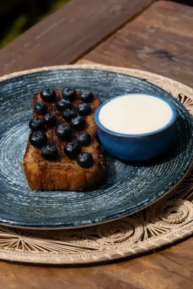 Postre artesanal de pan brioche caramelizado con arándanos frescos y crema, servido en el restaurante del Hotel Aimarawa Palomino, una experiencia gastronómica de lujo frente al mar.