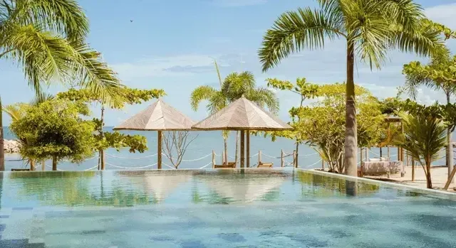 Piscina del Hotel Aimarawa con vista al mar Caribe, rodeada de palmeras y sombrillas de palma en un entorno tropical de lujo.