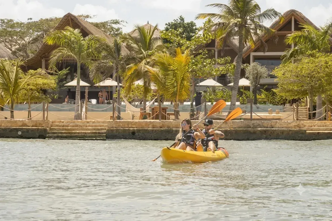 pareja haciendo Kayak frente a Aimarawa, hotel en San Antero, con cabañas, palmeras, mar tranquilo y día soleado