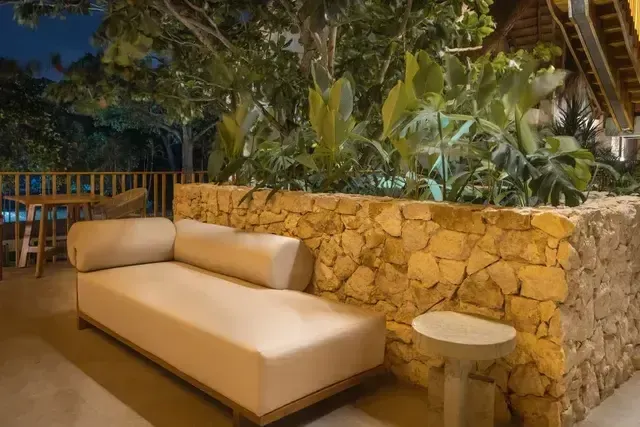 Terraza lounge del Hotel Aimarawa en San Antero con sofá moderno, muros en piedra natural y vegetación tropical para un ambiente exclusivo de descanso.