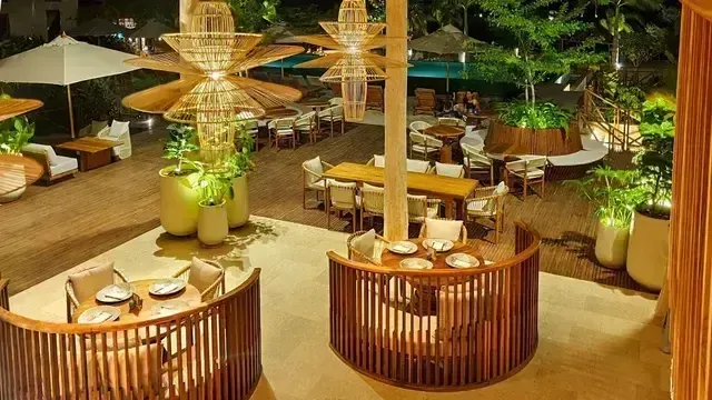 Restaurante al aire libre del Hotel Aimarawa con mesas circulares de madera, lámparas artesanales y vista a la piscina, rodeado de vegetación tropical.