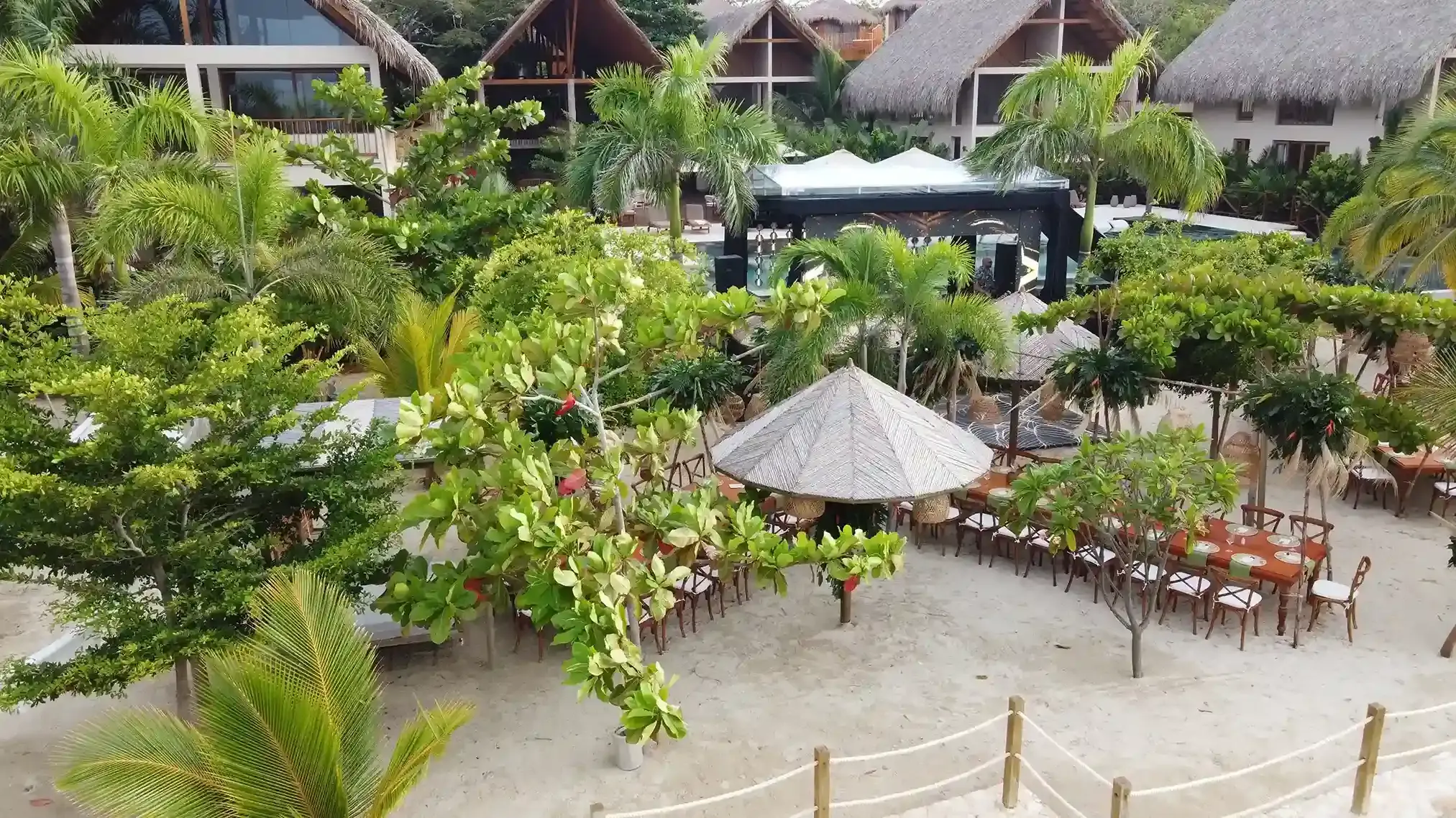 Montaje de mesas para matrimonio en la playa bajo quioscos de paja y palmeras en el Hotel Aimarawa.