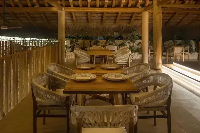 Restaurante del Hotel Aimarawa con mesas de madera, sillas artesanales y decoración natural bajo techo de palma, creando un ambiente cálido y acogedor.