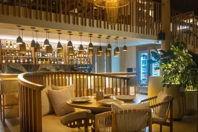 Bar y restaurante del Hotel Aimarawa en San Antero con mesas circulares de madera, ambiente elegante e iluminación cálida para experiencias culinarias de lujo.