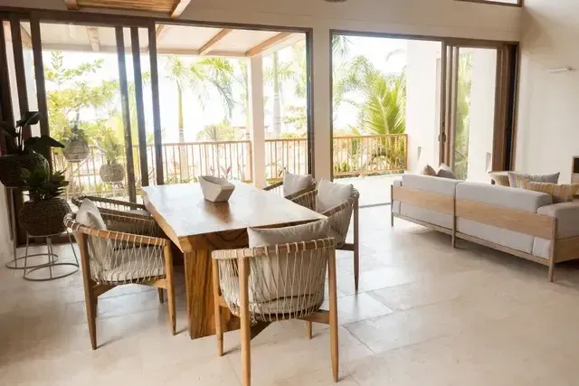 Sala comedor del Hotel Aimarawa San Antero con mobiliario en madera, sillas artesanales y ventanales con vista a palmeras y jardines tropicales.