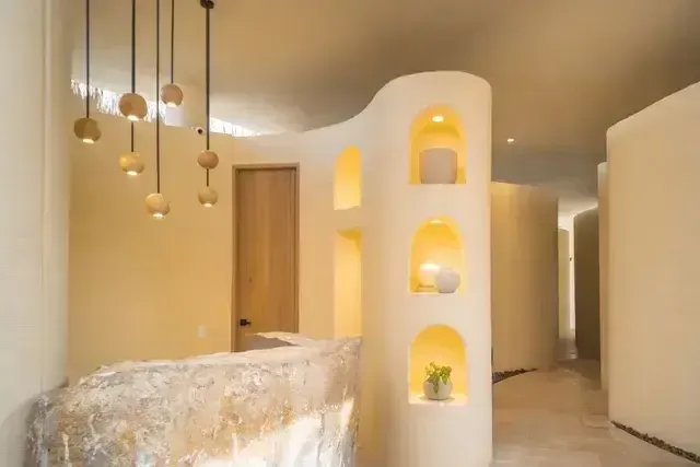 Interior del spa en el Hotel Aimarawa con diseño orgánico, paredes curvas en tonos cálidos, estantes iluminados con piezas decorativas y recepción en piedra natural.