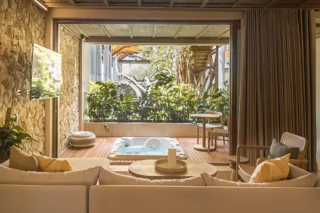 Suite del Hotel Aimarawa con sala acogedora, decoración en piedra natural y terraza privada con jacuzzi rodeado de vegetación tropical.